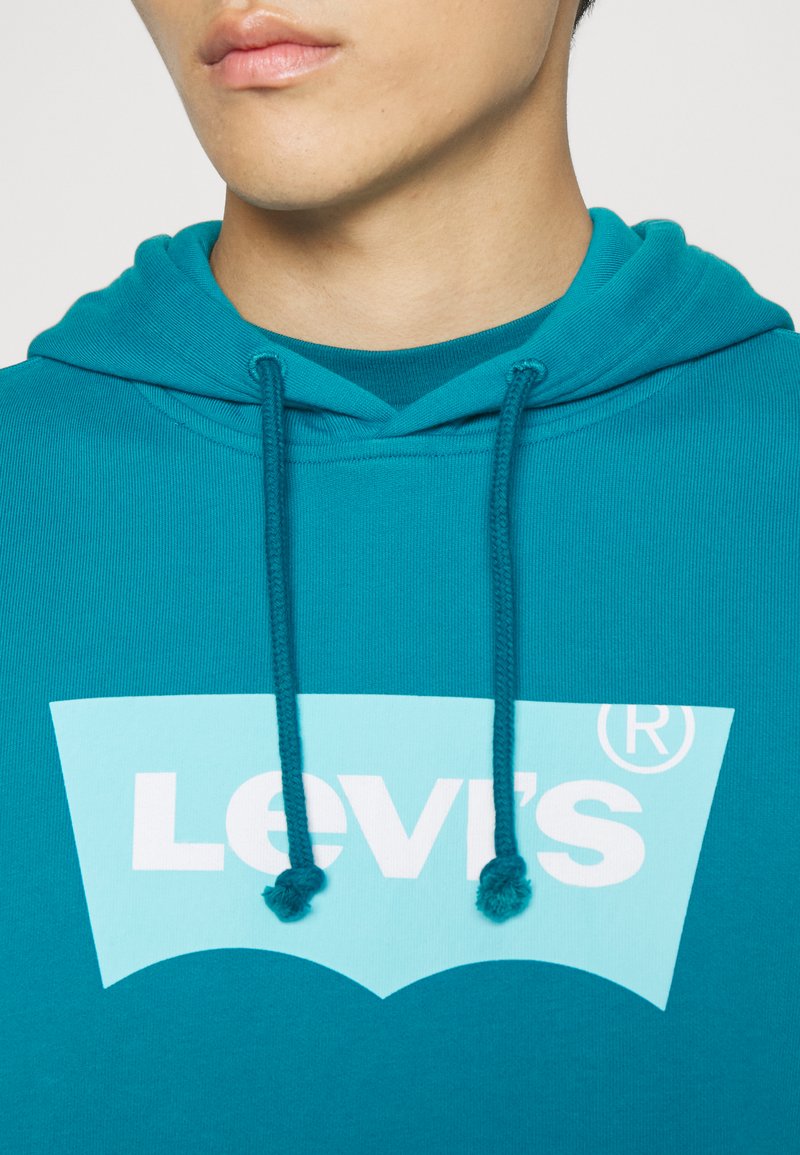 Sudadera con capucha de color verde azulado con una textura suave. Gran logo de Levi's en azul claro en la parte frontal, que presenta un diseño curvado clásico. Cuerdas ajustables.