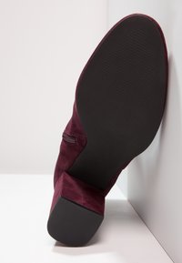 Bottine en suède bourgogne avec un bout carré, une fermeture éclair sur le côté et une semelle en caoutchouc noir texturé. Talon bloc bas pour la stabilité.