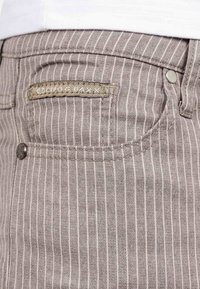 Gros plan sur une poche de pantalon gris à rayures fines avec un bouton en métal et une petite étiquette en tissu.