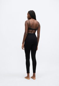 Sorte leggings med tætsiddende design, høj talje og ankelslids. Bæres med en matchende sort bh; glat tekstur og holdbart materiale.