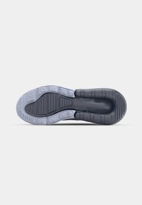Semelle de chaussure avec une bande de roulement noire et gris clair, comportant des motifs de grip texturés et des zones de coussins segmentées, sur un fond gris neutre.