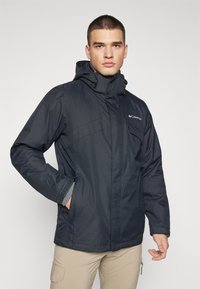 Black outdoor jacket with a high collar, adjustable hood, zippered pockets, and gray inner lining. Made of a lightweight, water-resistant material.