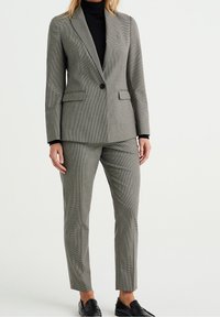 Grå rutig kostym med en figurnära kavaj med snedskurna slag och matchande smala byxor; slätt tyg och minimalt design.