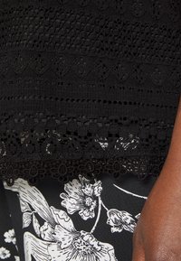Black fabric with textured patterns, featuring intricate lace detailing at the bottom. Floral pattern in white on the underlying fabric.