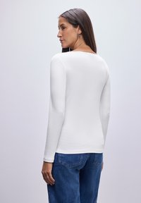 Hvid langærmet top med en rund halsudskæring, lavet af letvægtigt stof, parret med blå denim jeans med lommer og en afslappet pasform.