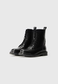 Pair of black leather combat boots with laces and side zippers on white background.