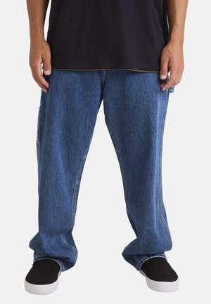 Blue denim baggy pants with a straight cut, visible stitching, and side pockets, paired with black sneakers.