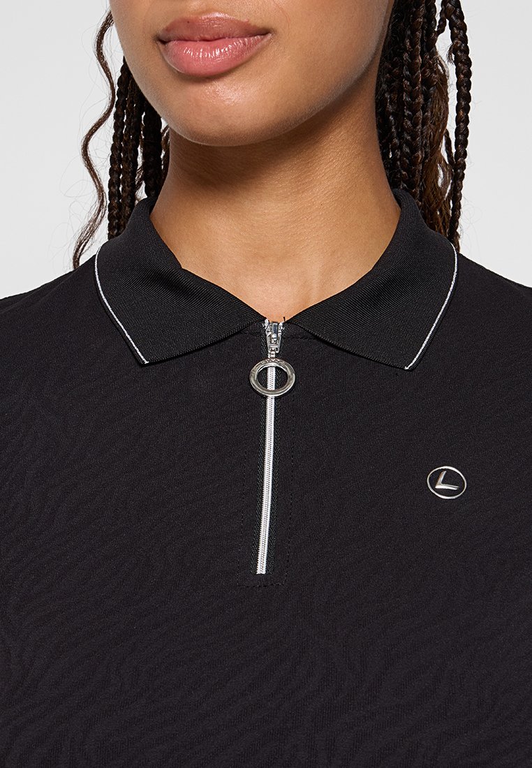 Polo noir avec un motif texturé, garniture blanche au col et fermeture éclair argentée. Présente un petit logo circulaire sur la poitrine gauche.