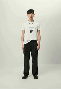 T-shirt branca com um design gráfico de um personagem, combinada com calças largas pretas e texturizadas. Calçado preto completa o conjunto.