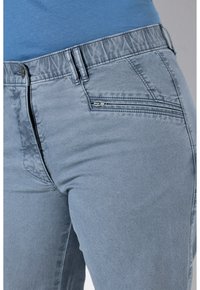 Pantaloni in denim azzurro chiaro con una texture liscia, dotati di una vita elastica e una tasca con zip sul lato.