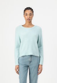 Lyseblå, myk genser med rund hals, lange ermer og avslappet passform. Kombinert med blå høytlivsjeans, med minimal detalj og tekstur.