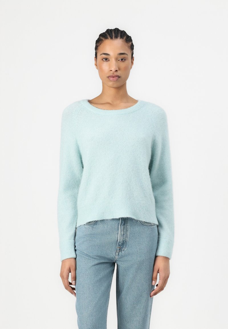 Lyseblå, myk genser med rund hals, lange ermer og avslappet passform. Kombinert med blå høytlivsjeans, med minimal detalj og tekstur.