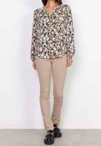 Bloemmotief lange mouw blouse in zwart, taupe en blauwe tinten, gecombineerd met beige slim-fit broek en zwart platform instappers.