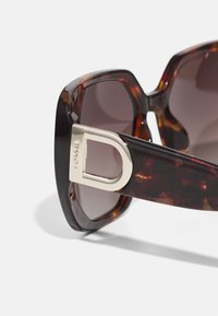 Lunettes de soleil en écaille de tortue avec des verres sombres, présentant un accent métallique doré sur le côté. Design de monture audacieux et épais avec une finition lisse.