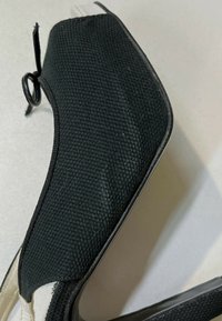 Chaussure en tissu noir texturé avec un bout pointu et une semelle fine sur un fond clair.