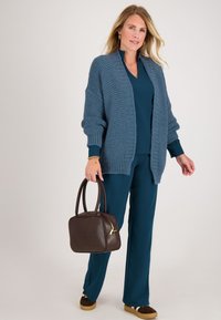 Gehaakt blauwe cardigan, teal top, bijpassende broek, bruine handtas, gouden accenten en bruine schoenen met lichte zolen. Ontspannen pasvorm en textuurstof.