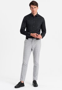 Camicia nera a maniche lunghe abbinata a pantaloni slim-fit grigio chiaro a quadri e sneakers nere.