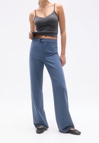Crop top gris côtelé avec bordure en dentelle, associé à un pantalon bleu taille haute à jambes larges avec fermeture à boutons et poches latérales.