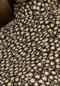 Zwarte trui met col, versierd met kleine gele bloemen. Zachte stof met een aansluitende pasvorm, die het bloemenpatroon mooi benadrukt.