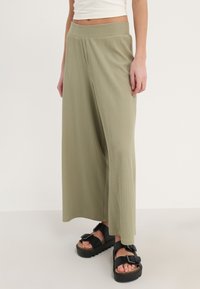 Olijfgroene wijde broek van ribbelstof, met een rekbare tailleband en gedetailleerde stiksels, gecombineerd met zwarte platform sandalen.