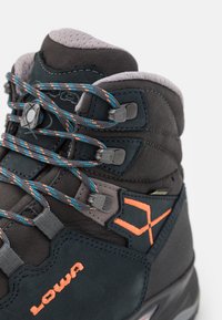 Botte de randonnée gris foncé avec des accents orange, dotée d'un matériau en suede texturé, de lacets durables et d'un design de cheville renforcé.