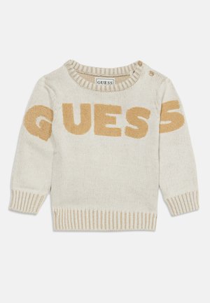 Pull en maille crème pour tout-petit avec poignets, encolure et bas côtelés beige, avec "GUESS" en grandes lettres beige sur la poitrine et les manches.