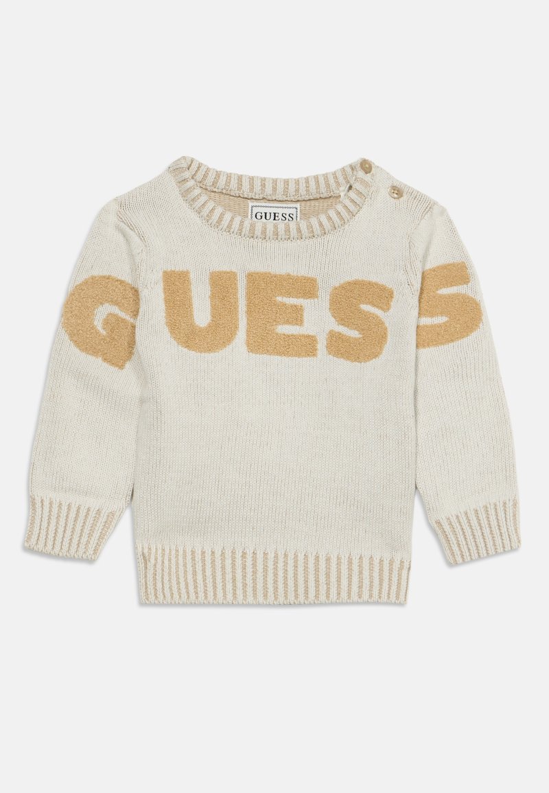 Pull en maille crème pour tout-petit avec poignets, encolure et bas côtelés beige, avec "GUESS" en grandes lettres beige sur la poitrine et les manches.