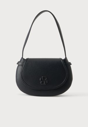 Femme portant un haut à manches longues marron foncé, un pantalon beige à jambes larges, des sandales à talons noires, tenant un sac à épaule noir.