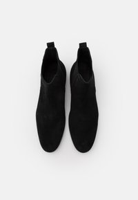 Botas de tobillo de ante negro con una textura suave, paneles laterales elásticos y tiradores para facilitar su colocación. Punta redondeada y diseño minimalista.
