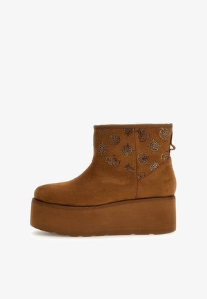 Botte cheville en daim marron avec motifs métalliques décoratifs, bout rond, semelle plateforme épaisse et texture douce. Dotée d'une languette à l'arrière.
