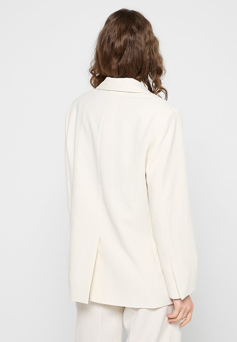 Weißes strukturiertes Blazerjacke mit einem leicht übergroßen Schnitt, Reverskragen, langen Ärmeln und einem Schlitz an der Rückseite. Schlichtes und modernes Design.