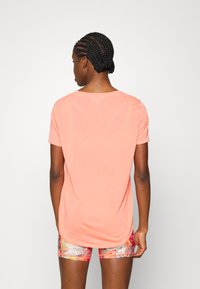 T-shirt de manga curta laranja claro com decote redondo e um corte solto, combinado com calções coloridos e com padrões.