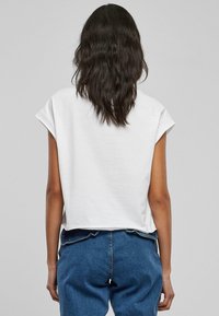 Top corto bianco in cotone a maniche corte con maniche arrotolate, abbinato a jeans in denim blu. Il retro è semplice con una vestibilità rilassata.