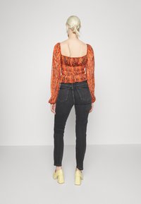 Camisola de mangas compridas, ajustada, em padrão de cobra laranja com decote quadrado, combinada com jeans escuros de cintura alta e saltos robustos amarelos.