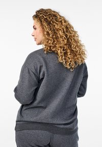 Felpa grigia realizzata in materiale morbido con una vestibilità comoda. Presenta polsini e orlo a costine, e una texture liscia. Vista da dietro.