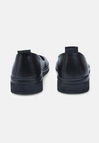 Zapatos de cuero negros con una textura suave, forma redondeada, tacón bajo y tiradores en la parte posterior, con un detalle de costura minimalista.
