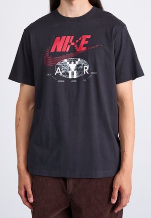T-shirt en coton noir avec un grand logo Nike rouge, design graphique de globe avec le texte blanc "AIR" et "TOUTES LES ROUTES MÈNENT AU SPORT." Manches courtes, col rond.