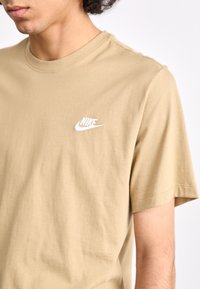 Kreminė medvilninė marškinė su apvaliu iškirpimu ir trumpomis rankovėmis. Ant kairiojo krūtinės ploto yra balta išsiuvinėta Nike logotipas. Minkšta tekstūra.