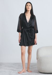 Mustast satiinist hommikumantel pitsist varrukatega, millel on seotud vöökoht, põlveni ulatuv lõige ja sile tekstuur. Kandmise all heleda tooniga pluus.