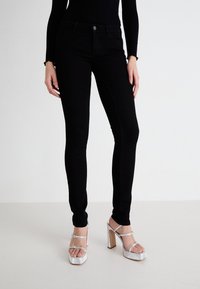 Jeans negri skinny cu o textura netedă, talie înaltă și cinci buzunare, asortați cu sandale argintii cu toc înalt și bretele pentru gleznă.