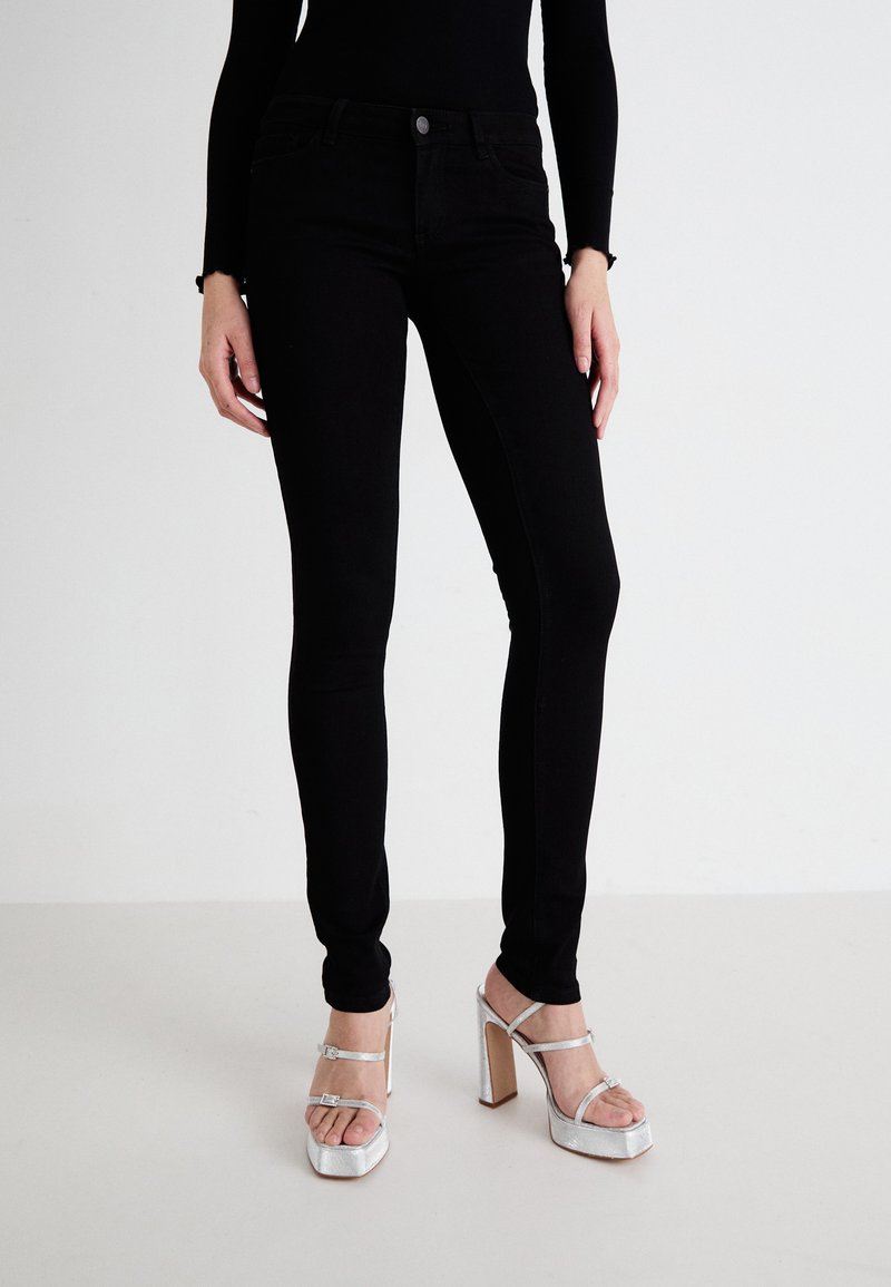 Jeans negri skinny cu o textura netedă, talie înaltă și cinci buzunare, asortați cu sandale argintii cu toc înalt și bretele pentru gleznă.