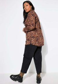 Maglietta con stampa leopardata in tonalità di arancione e nero, abbinata a jeans in denim scuro. Scarpe nere chunky con accenti borchiati.