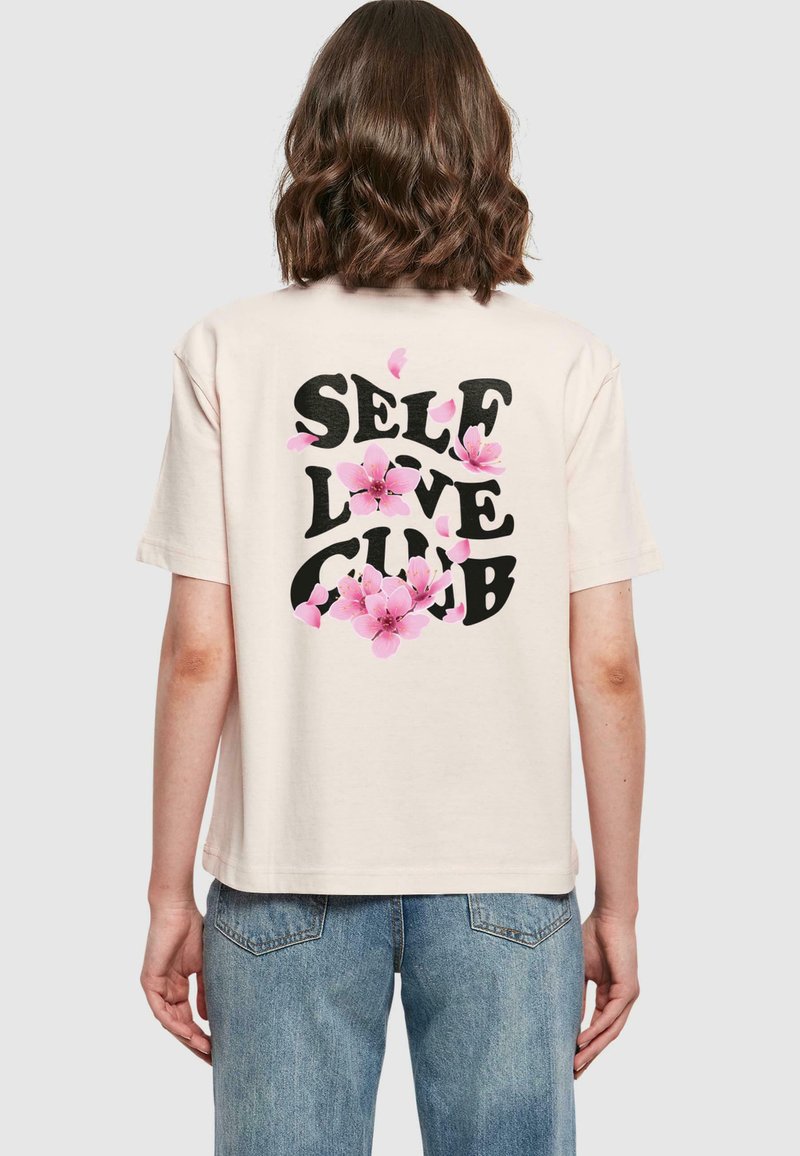 Krem majica od pamuka s crnim grafičkim natpisom "SELF LOVE CLUB" ukrašena ružičastim cvjetnim ilustracijama na leđima.