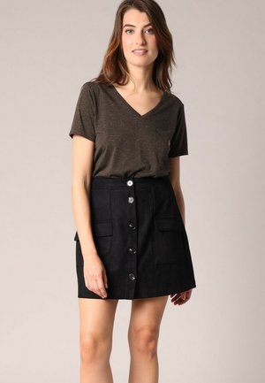 Jupe en daim noir avec un devant boutonné, deux poches latérales et une coupe ajustée, assortie à un t-shirt brun à col en v.