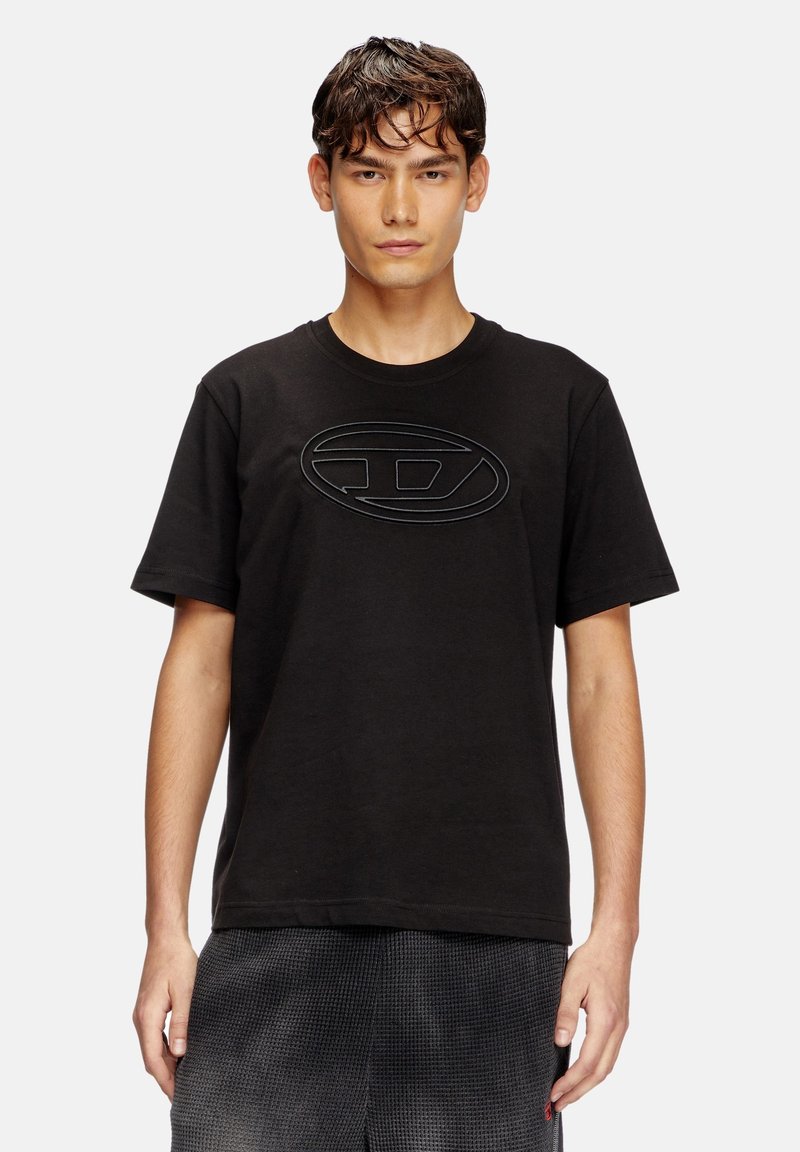 T-shirt en coton noir avec un col rond, des manches courtes et un logo en relief au centre. Présente une coupe décontractée et une texture lisse.