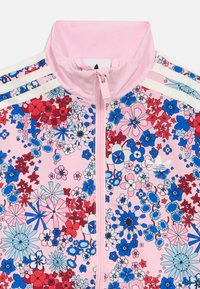 Giacca sportiva con stampa floreale caratterizzata da una base rosa, fiori blu e rossi, colletto alto e dettagli a righe bianche sulle spalle. Chiusura con cerniera.