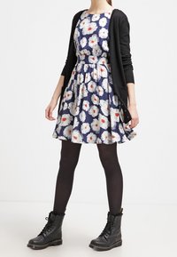 Abito floreale con sfondo navy, fiori bianchi e arancioni, gonna svasata. Abbinato con un cardigan nero e stivali nero con lacci.