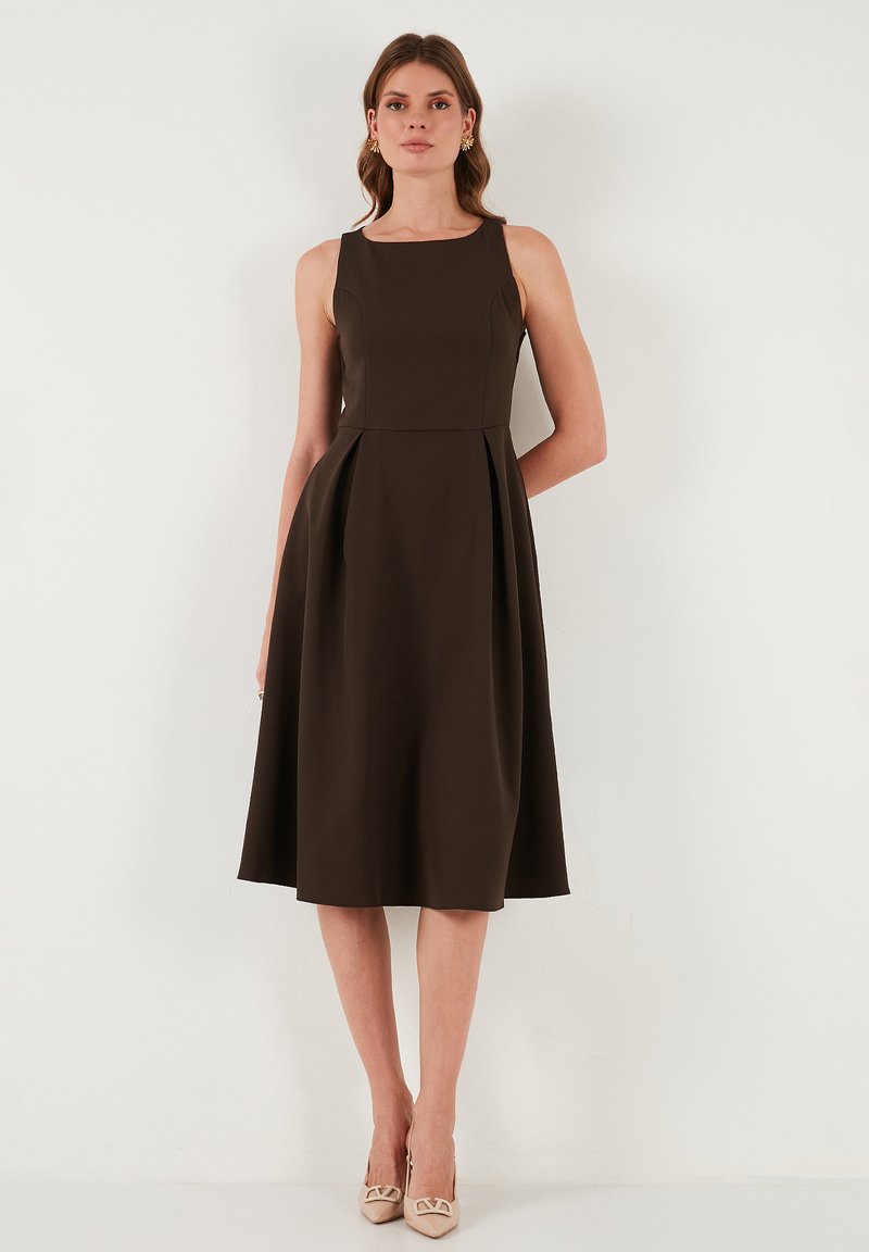 Brązowa bezrękawnikowa sukienka w kształcie litery A z dopasowanym gorsetem i plisowaną spódnicą. Gładka tekstura, do kolan, w zestawie z beżowymi szpilkami.