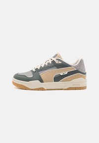 Botte de sport avec une tige en cuir vert, des accents beige et gris, des détails texturés, un col rembourré et une semelle extérieure en caoutchouc caramel.
