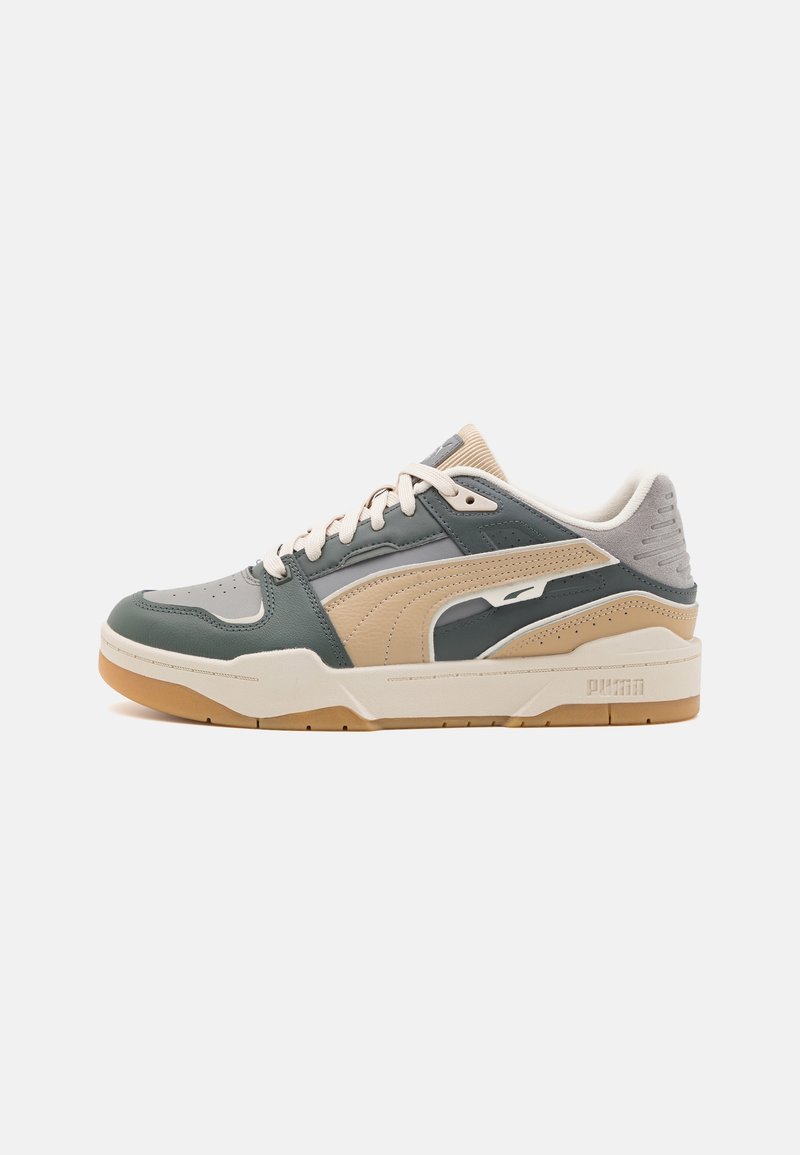 Botte de sport avec une tige en cuir vert, des accents beige et gris, des détails texturés, un col rembourré et une semelle extérieure en caoutchouc caramel.